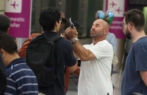 Un rico empresario condenado por violar a una mujer en un club de Mykonos intenta agarrar el teléfono de un periodista después de ser confrontado en el aeropuerto de Sydney